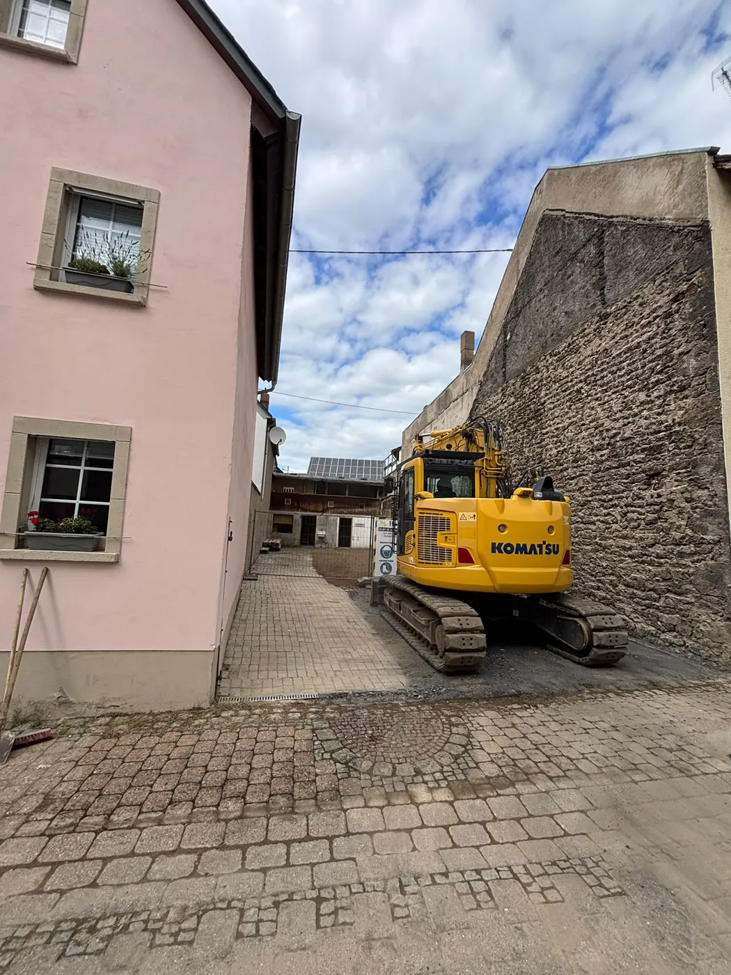 Bagger in der schmalen Gasse zwischen Nachbarhaus und Bruchsteinmauer in Ochtendung