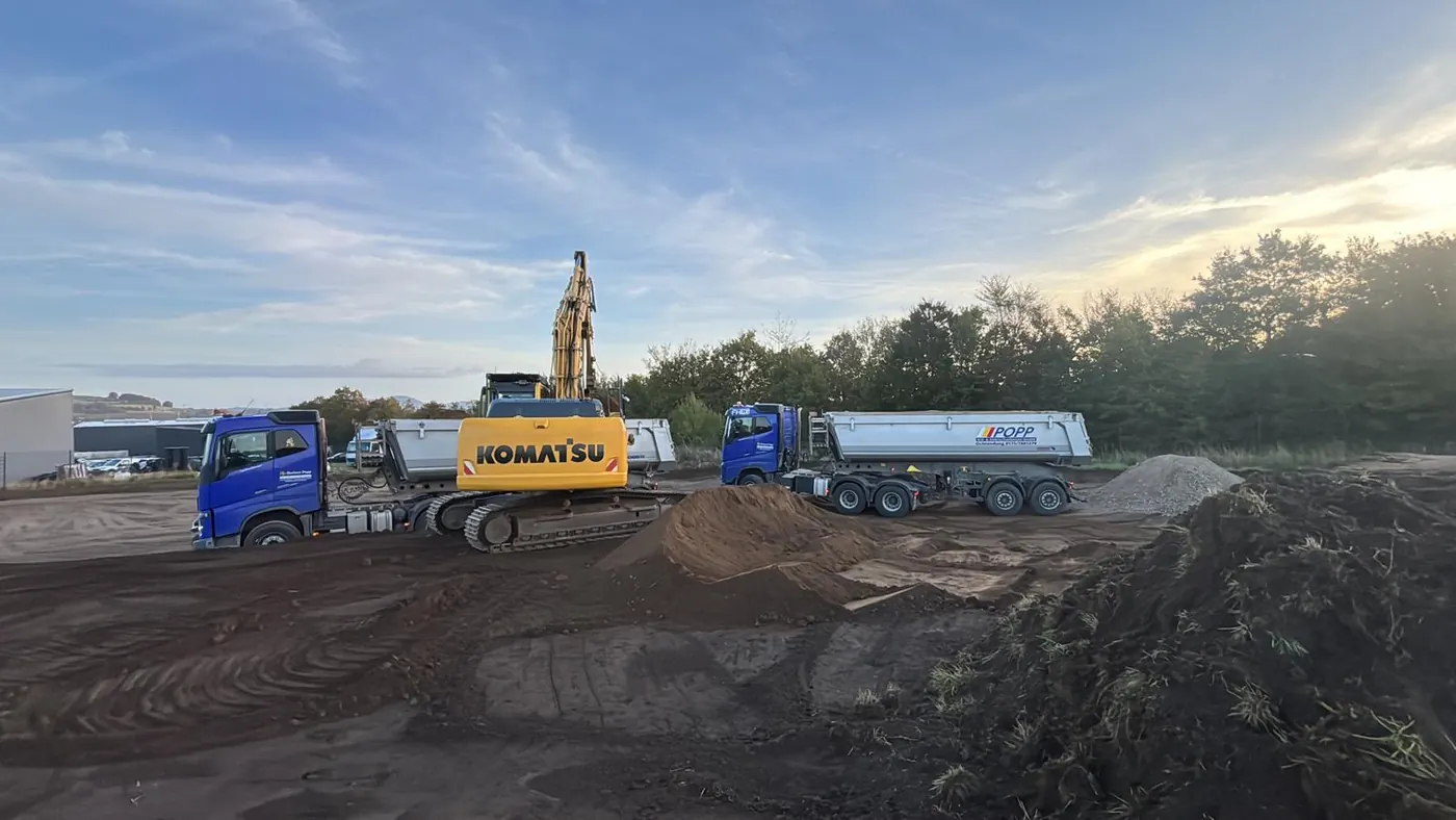Komatsu Kettenbagger lädt Erdaushub für die Lagerhalle auf Sattelkipper